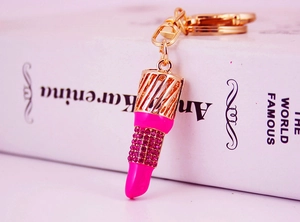 Close-up of a lipstick keychain with pink rhinestones and a gold metal frame on a book