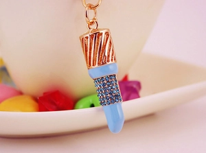 Detailed view of lipstick keychain featuring sparkling blue rhinestones and gold accents