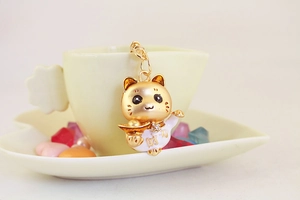 Détail du pendentif Maneki Neko doré avec strass et caractères porte-bonheur sur tasse