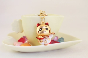 Détail macro d'un porte-clés Maneki Neko doré représentant un chat porte-bonheur et un lingot