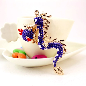 Golden dragon keychain with blue rhinestones and enamel hanging on a ceramic cup edge