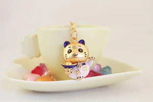 Détail d'un porte-clés Maneki Neko doré avec strass et lingot de chance sur une tasse