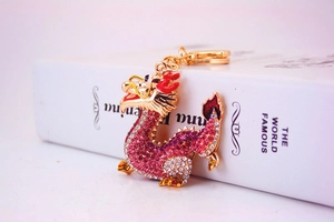 Close-up of golden dragon keychain with pink and white rhinestones on a book background