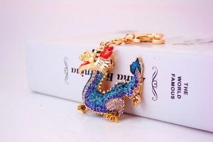 Detail view of a gold Chinese dragon keychain with blue rhinestones on a white book