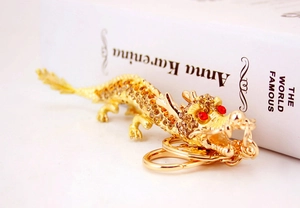 Détail d'un porte-clés dragon doré orné de strass orange sur un livre blanc pur
