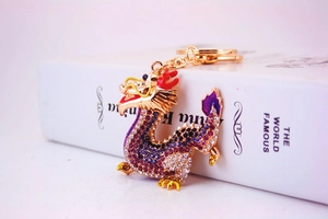 Detailed close-up of a golden metal dragon keychain with purple and pink rhinestones