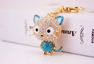 Close-up of golden cat keychain with white and sky blue sparkling crystals on a white book