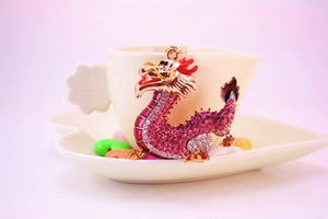 Detail of pink crystal dragon keychain with gold plating resting on a white coffee cup