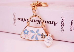 Detailed view of handbag-shaped keychain with gold metal frame and blue floral accents