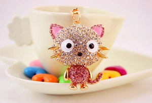 Detail of crystal cat keychain with pink rhinestones on a white ceramic cup