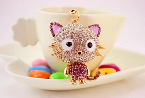 Detail of cute cat crystal keychain with purple rhinestones on a beige cup