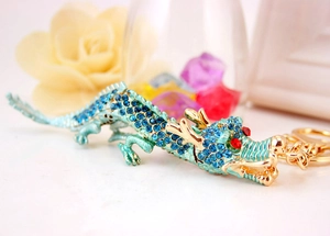 Détail du porte-clés dragon avec strass bleus et finition dorée sur un fond de fleurs