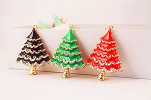 Detailed close-up of three enamel rhinestone Christmas tree charms in green, black, and red
