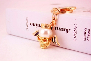Macro detail of a golden skull keychain with a pearl forehead and sparkling rhinestones