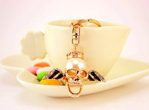 Detail of a golden skull keychain with pearl and wings on a white flower-shaped coffee cup