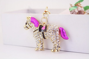 Close-up of golden horse keychain featuring white rhinestones and purple enamel details