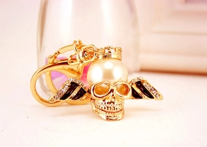 Detail of a gold skull keychain with a crown pearl and sparkling rhinestone wings