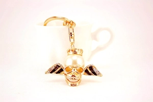 Detail of a gold skull keychain with crown, wings and large white pearl over a cup