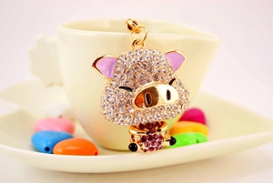 Dettaglio portachiavi a maialino dorato con strass rosa su sfondo tazza da caffè