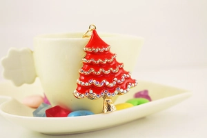 Detail of red enamel Christmas tree keychain with crystals on a white ceramic cup