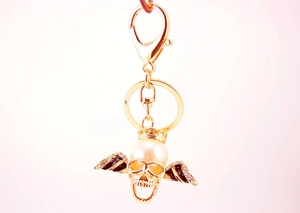 Detailed view of skull keychain with large pearl, crystal wings and gold finish