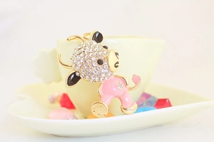 Close-up of cute pink enamel cow keychain with sparkling white rhinestones on a ceramic dish