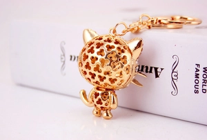 Macro detail of golden cat keychain with hollow clover pattern and pink crystal accents