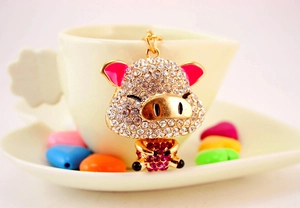 Dettaglio del portachiavi a maialino dorato con strass rosa su una tazza da caffè