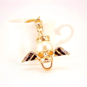 Golden pearl skull keychain with crown and rhinestone wings on a white cup edge