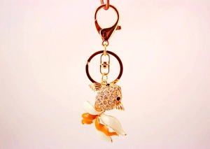 Détail du porte-clés poisson rouge avec cristaux blancs et émail sur un fond rose poudré