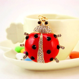 Charming red ladybug keychain with black crystals on a white ceramic cup edge
