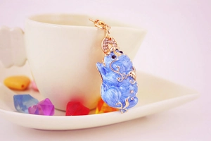 Macro view of blue enamel Pixiu keychain with rhinestones hanging on a white coffee cup