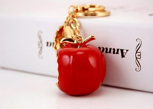 Close-up of red apple keychain with a gold leaf pendant on a metallic ring