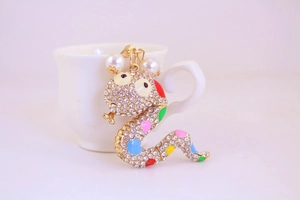 Detailed close-up of a golden snake keychain with rhinestones and pearls by a cup