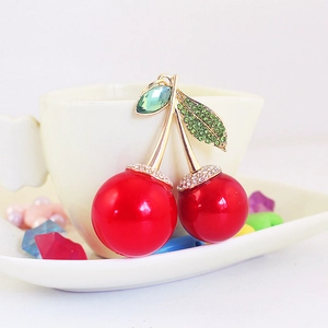 Sparkling cherry keychain with red spheres and green crystal leaves on a white cup