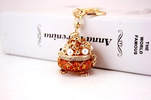 Detail of gold-plated lucky censer keychain with red enamel and pearl accents