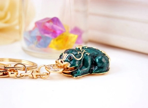 Macro shot of golden Pixiu keychain with green enamel and sparkling white zircons