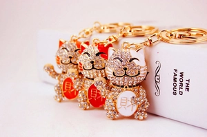 Close-up of crystal-studded fortune cat keychains in gold plating with red and white colors