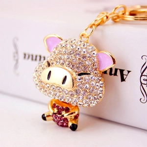 Sparkling crystal pig keychain accessory with pink ears and purple heart on white book
