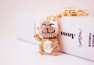 Close-up of golden Maneki Neko keychain with sparkling crystals and Cai character detail