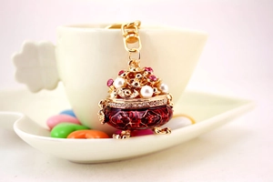 Miniature incense burner keychain with red enamel and pink rhinestones on a table