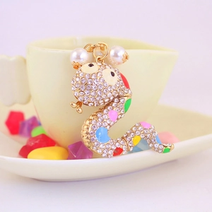 Golden snake keychain with colorful rhinestones and imitation pearls on a white ceramic cup