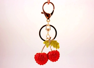 Detailed close-up of a sparkling red rhinestone cherry keychain with golden lobster clasp