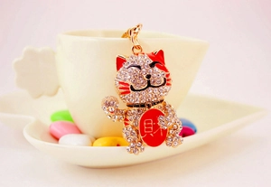 Close-up of golden Maneki Neko keychain with sparkling rhinestones and red details