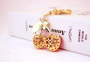 Detail of a golden metal cherry keychain with intricate hollow-out patterns and leaf detail