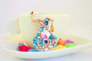 Close-up of golden money bag keychain with vibrant blue crystals on a ceramic cup