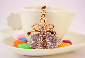 Close-up of golden bell keychain with white rhinestones and a bow on a white cup