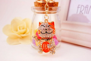 Detail of golden lucky cat keychain with orange enamel ears and sparkling crystals