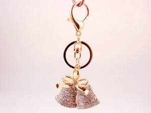 Close-up of golden double bell keychain featuring white crystals and a delicate bow detail