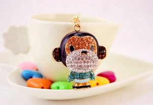 Close-up of sparkling rhinestone monkey keychain pendant with golden metal clip on a white cup